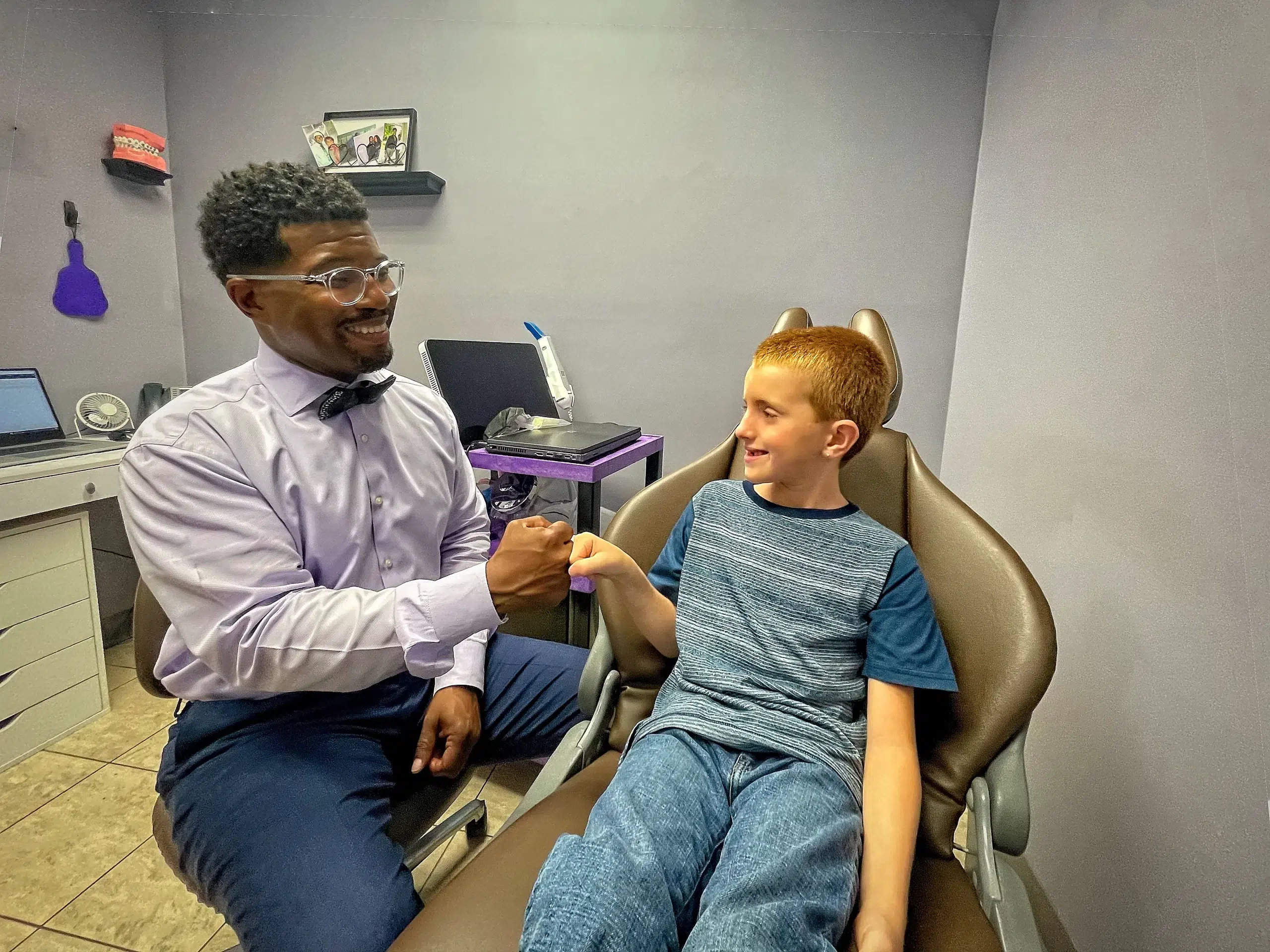 Dr. Romia Goff in a lavender shirt with a bowtie giving a young patient a fist bump