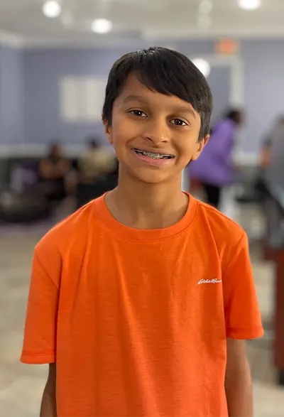 Portrait photo of child in orange shirt undergoing early orthodontic treatment with braces