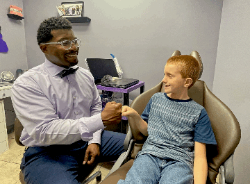 Dr. Romia Goff in a lavender shirt with a bowtie giving a young patient a fist bump