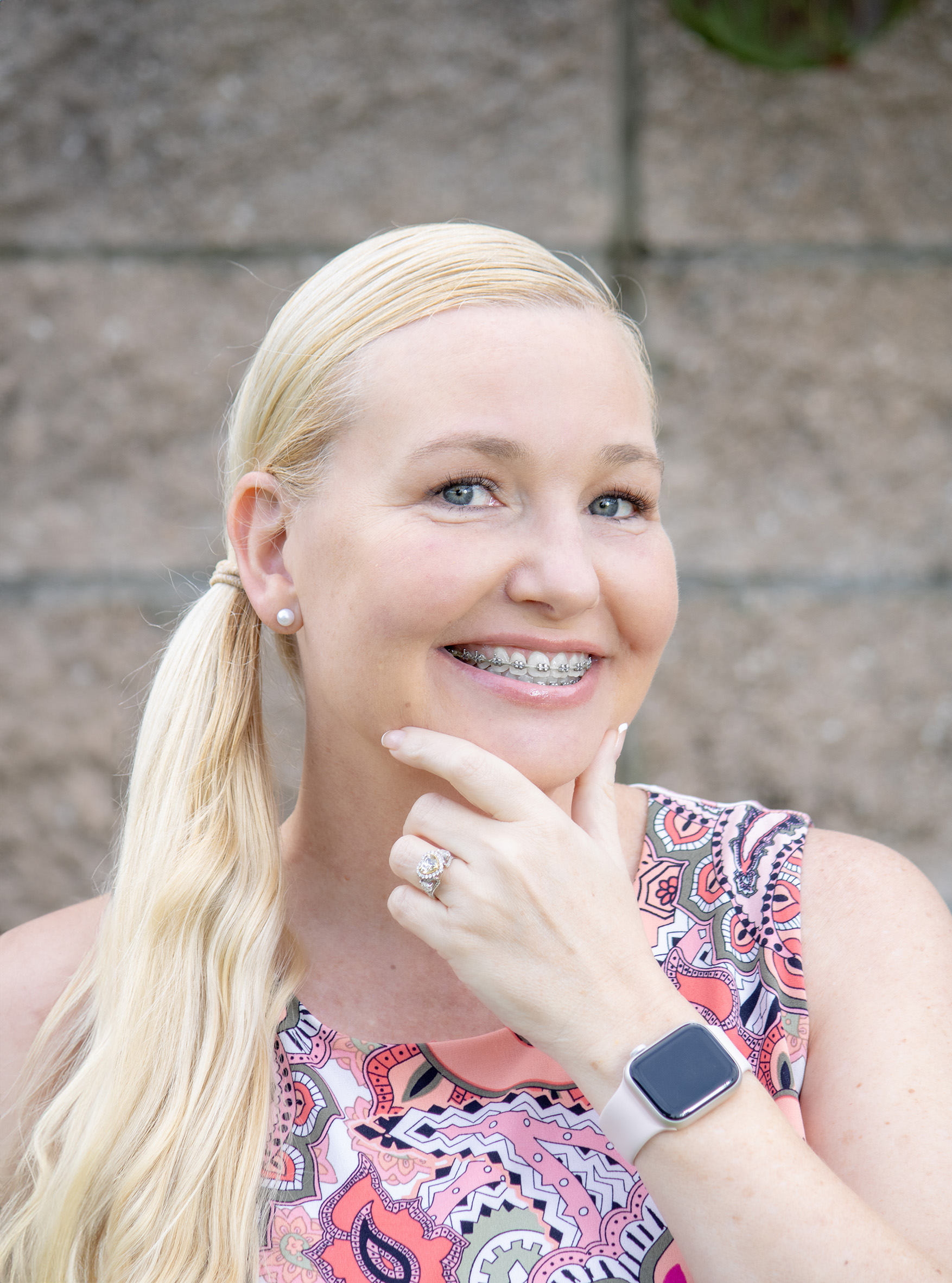 Blonde woman standing in front of a brick wall, showcasing her smile with braces.