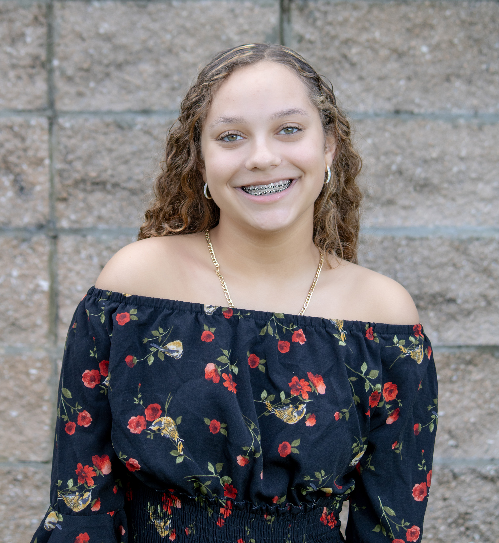 A teen wearing a dress, standing in front of a brick wall.