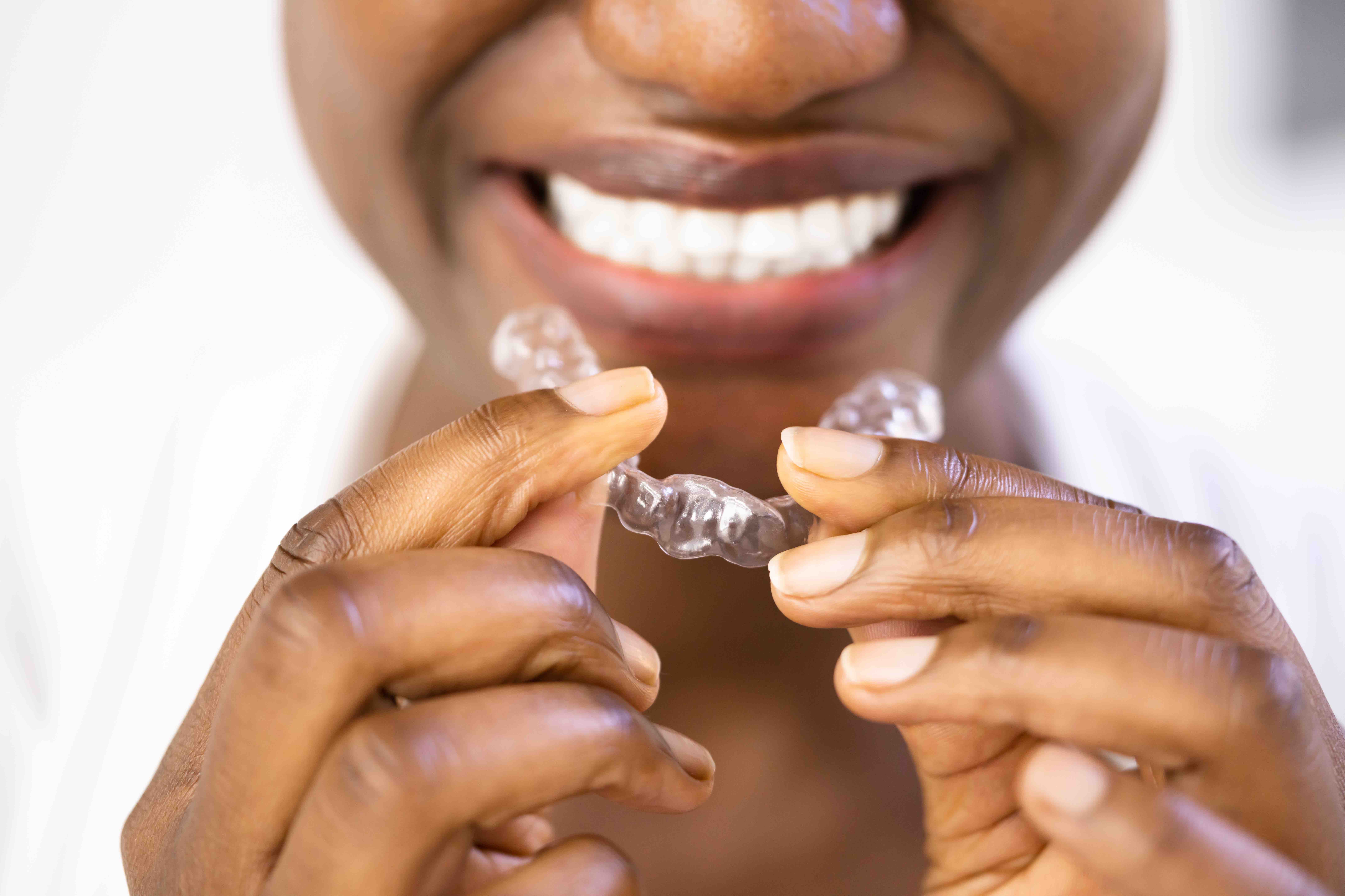 A smiling African American woman holding Invisalgin Retainer in front of her smile at Goff Orthodontics in Brevard County, FL.