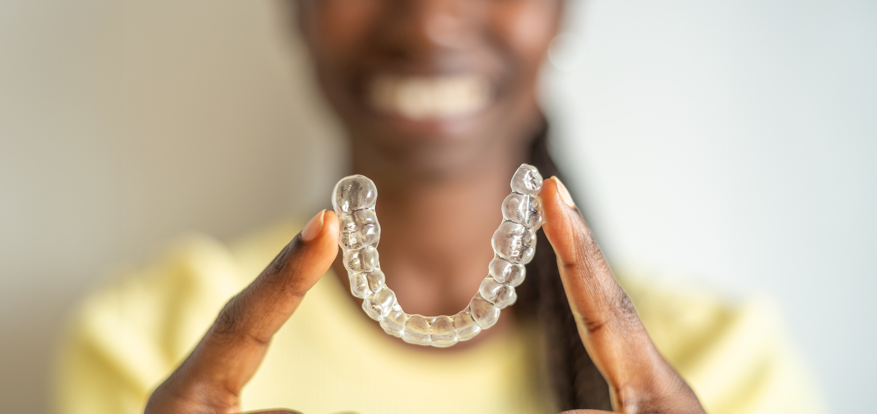 Young woman holding with two fingers an invisible dental aligner while smiling in Brevard County, FL.