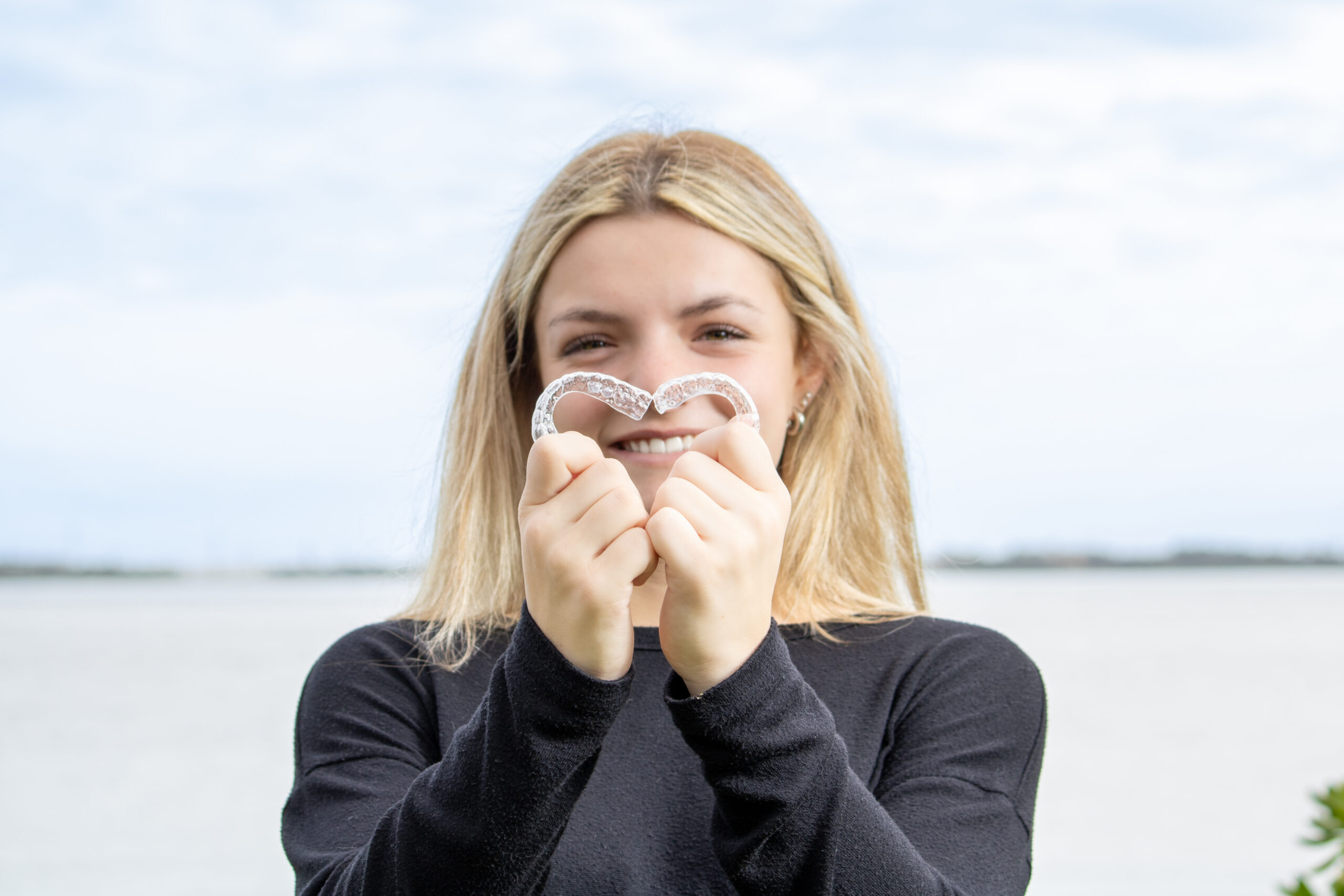 A smiling teenager holding an invisible teeth aligner at Goff Orthodontics in Brevard County, FL.