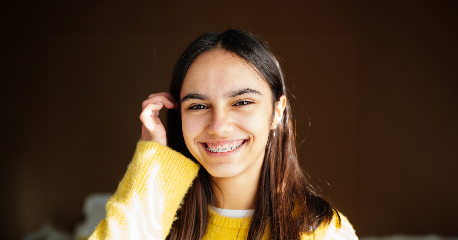 Radiant teen with braces in Melbourne, FL smiling and shifting her hair behind her ear.