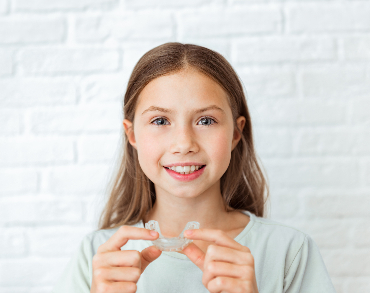 Girl undergoing interceptive orthodontic treatment with Invisalign First holding her aligners