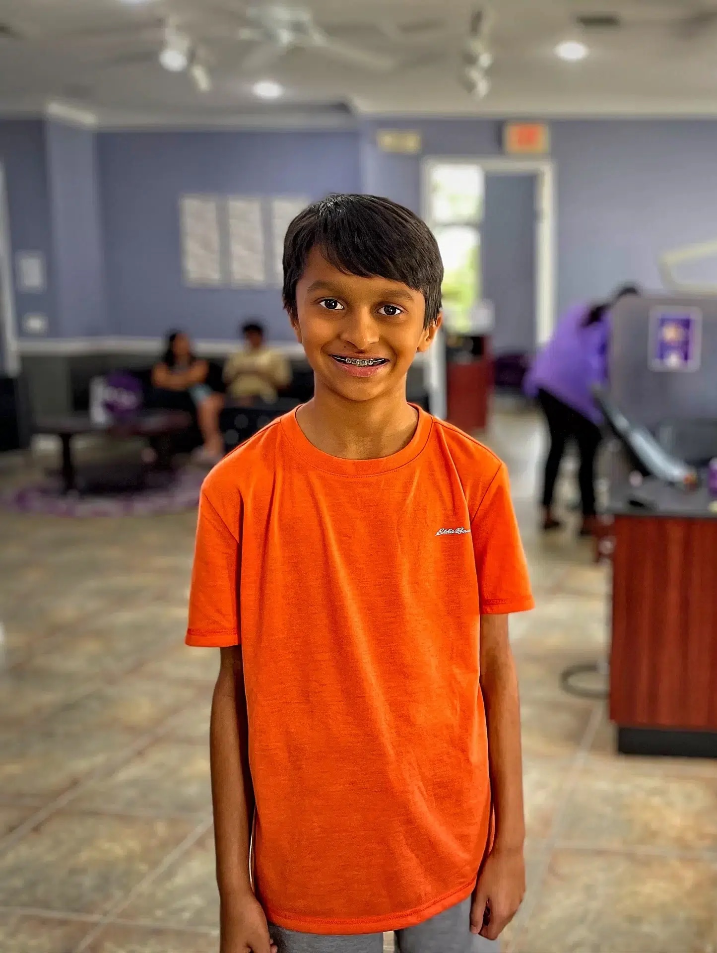 Smiling child undergoing early orthodontic treatment with braces wearing a bright orange shirt 