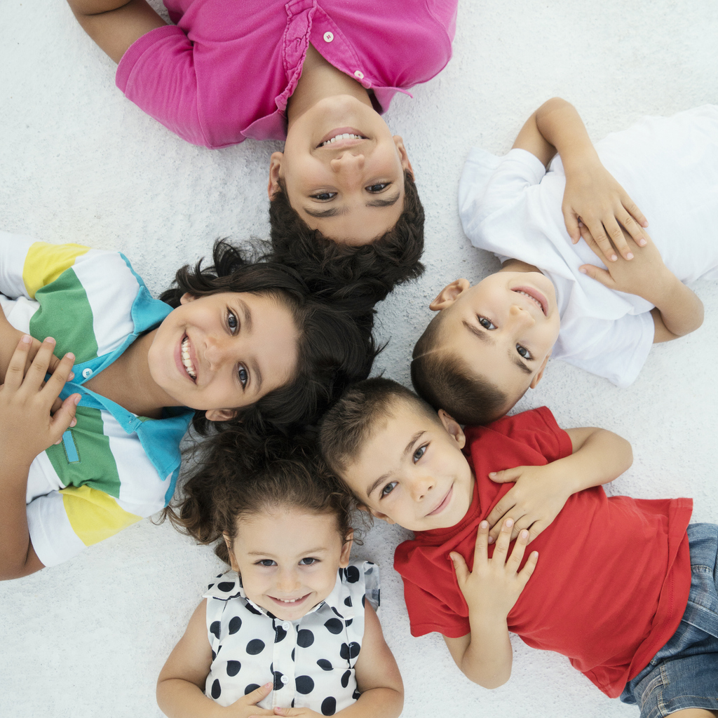 Group of children in different colored shirts smiling and lying in a circle